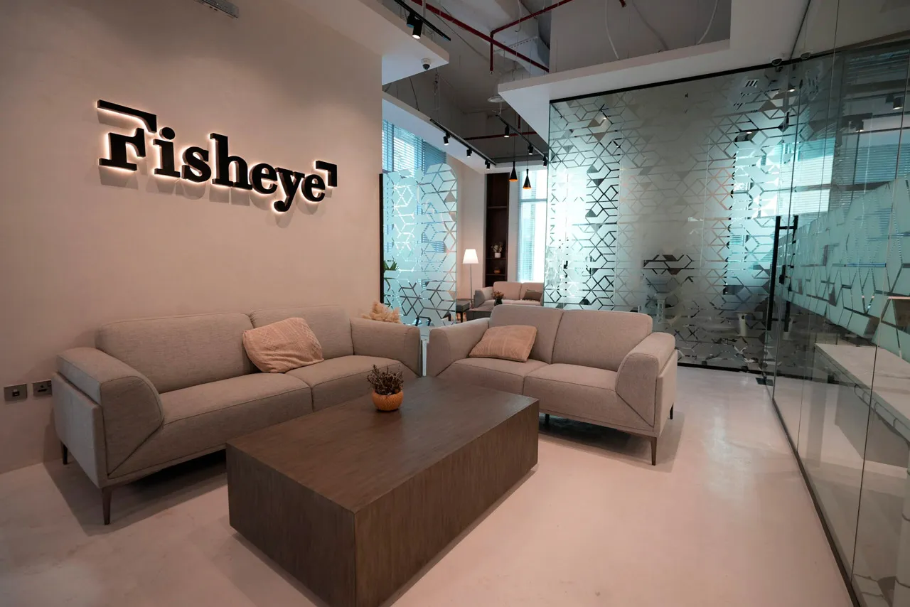 Fisheye waiting room: interior view of a modern office lounge featuring a light-colored sofa with cushions, a rectangular coffee table, and the brand name Fisheye illuminated on the wall.