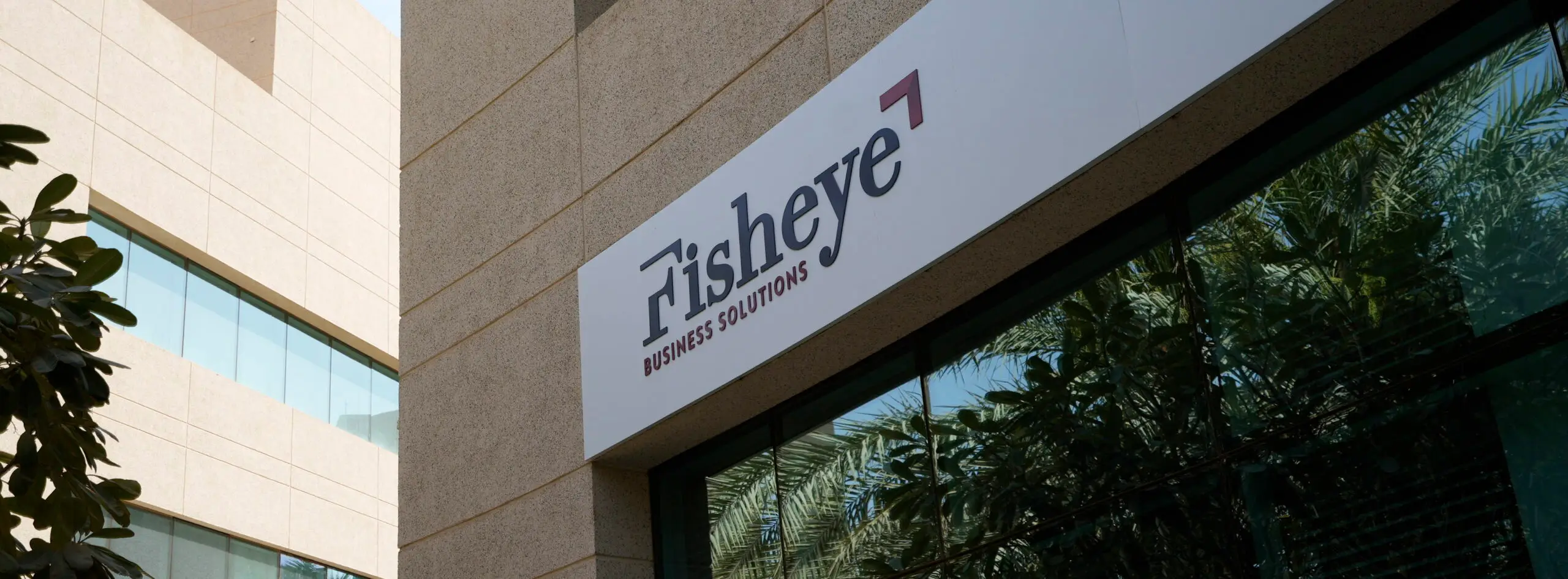 Fisheye logo outdoor: Signage of Fisheye Business Solutions on a glass facade with reflections of greenery and buildings.