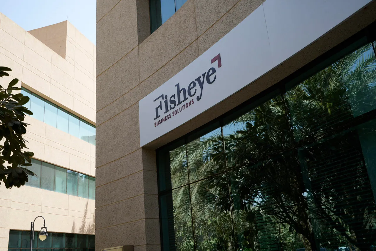 Fisheye logo outdoor: Signage of Fisheye Business Solutions on a glass facade with reflections of greenery and buildings.