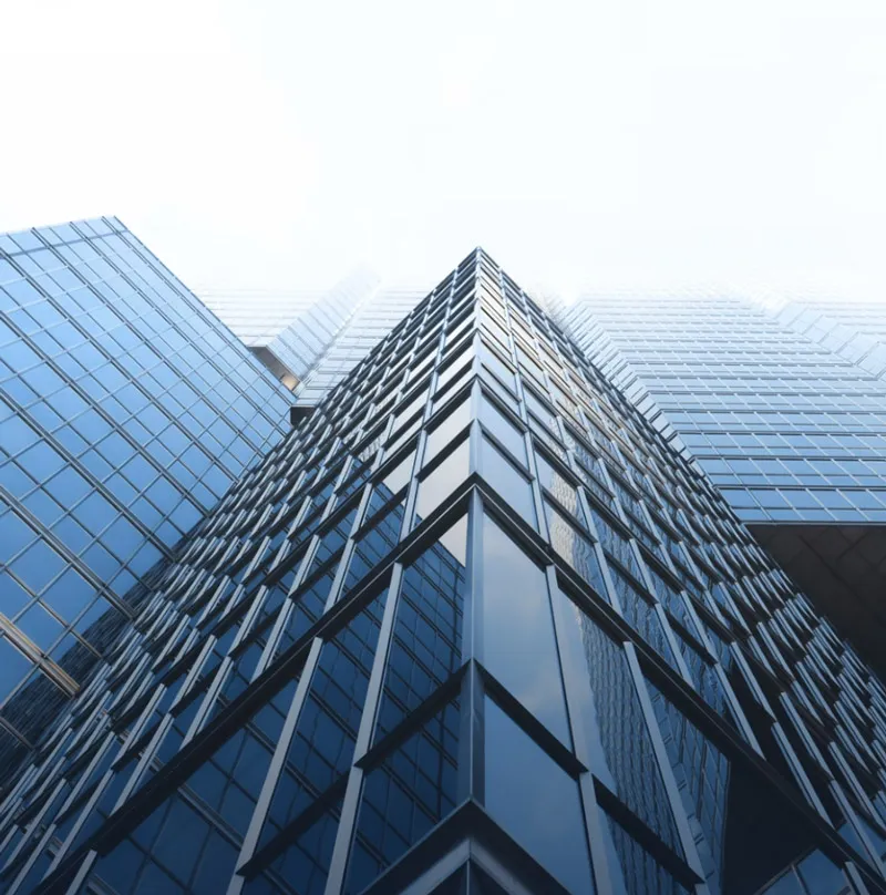 Looking up at a modern glass skyscraper with a sharp, angular design, showcasing reflective windows and a clear sky in the background.